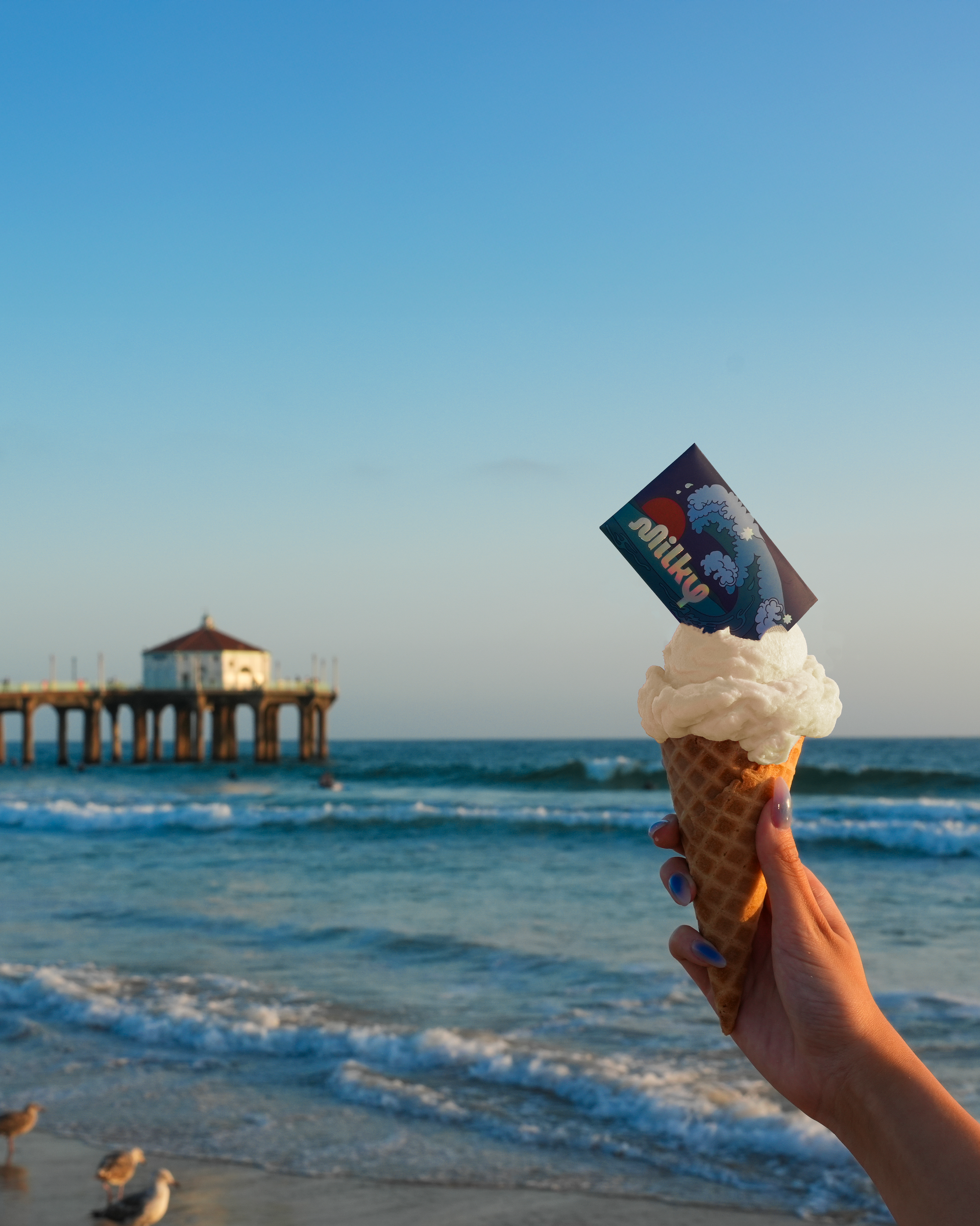 Ice cream cone with a card held up in front of a pier and ocean