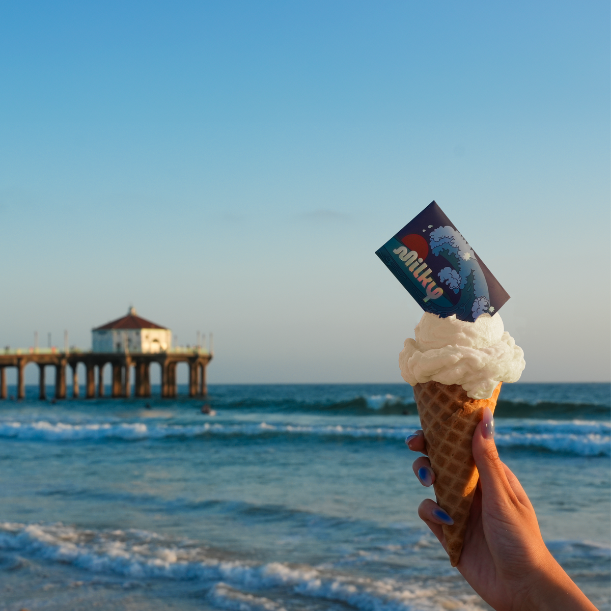 Ice cream cone with a Milky card on top against a beach and pier background